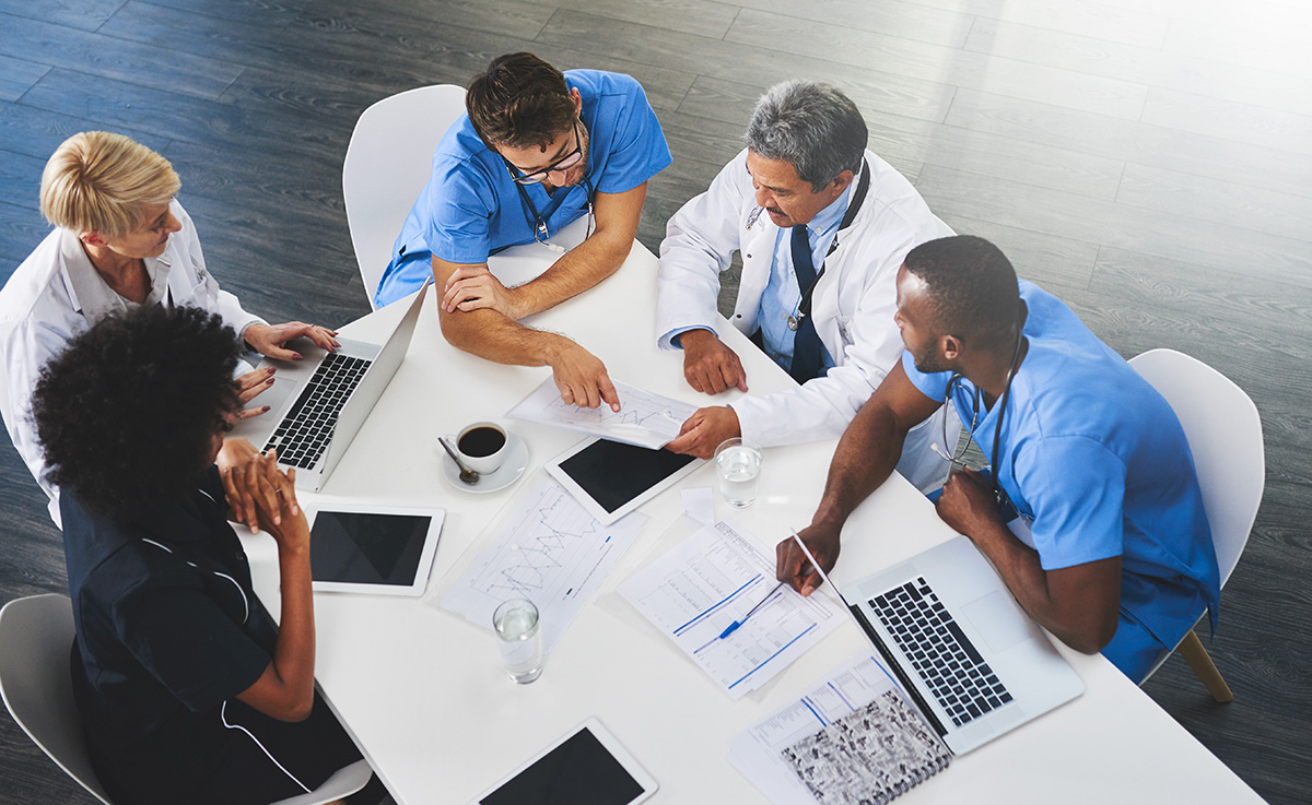 Team of medical workers sitting and meeting with laptops around table. Doctors and staff discussing papers and test results. Healthcare experts handling daily tasks and duties
